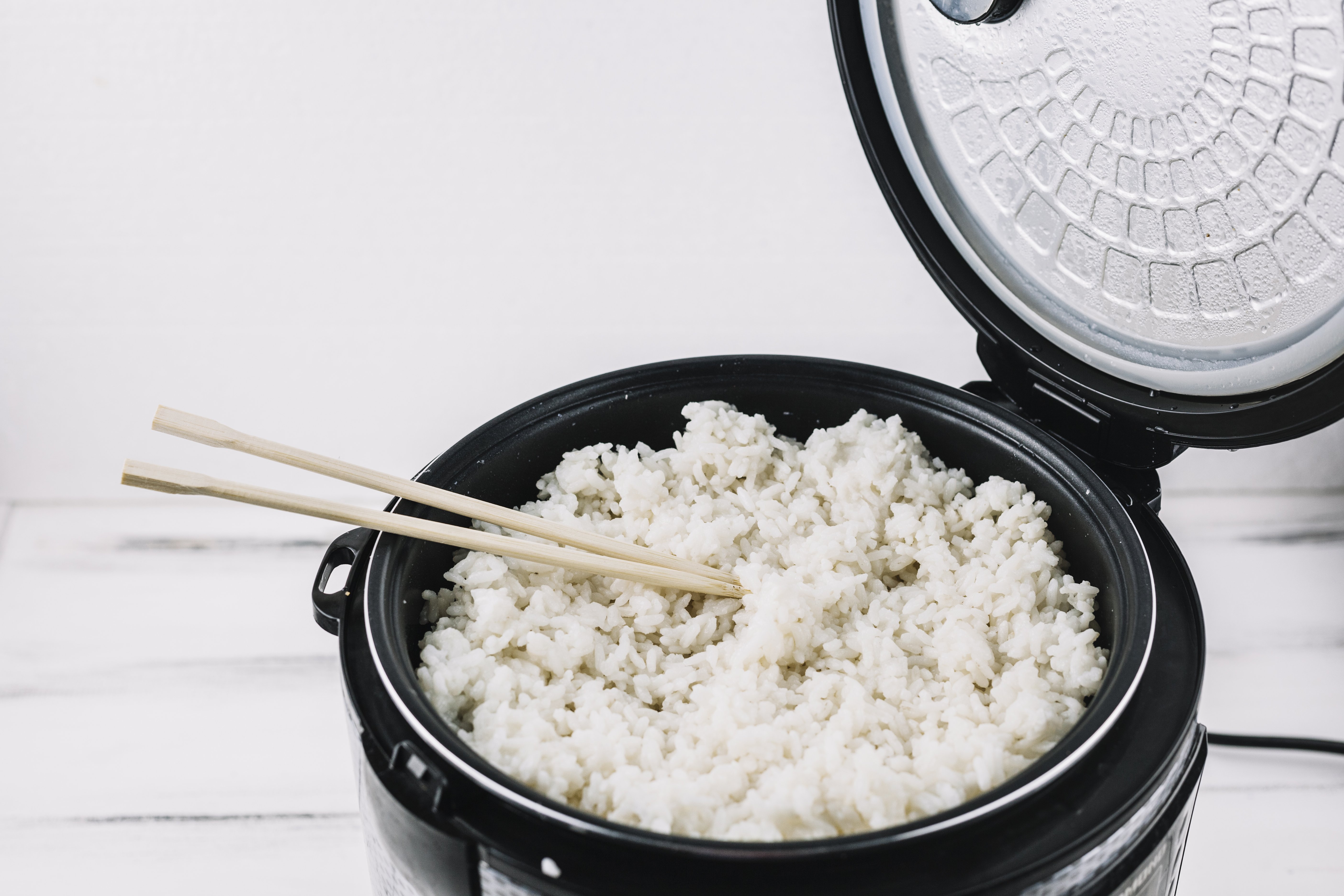 Cooked white rice in a rice cooker with chopsticks, ready to be cooled and chilled for Yangzhou fried rice
